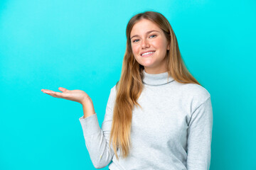 Young blonde woman isolated on blue background holding copyspace imaginary on the palm to insert an...
