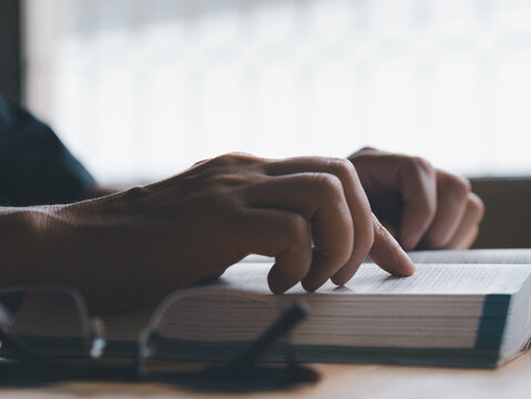 Reading book concept. Person reading a book in the work office or living room or library, he sitting on the wood table close to window. Finger point at the text letter in a book.