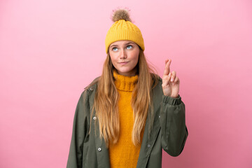 Young blonde woman wearing winter jacket isolated on pink background with fingers crossing and...