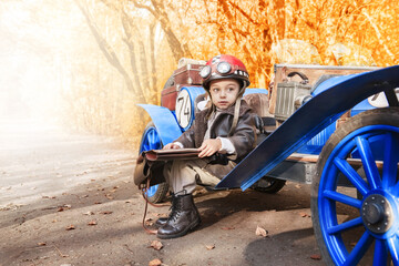 Young happy child. Little funny boy in the image of a racer started and plays an old racing car in...