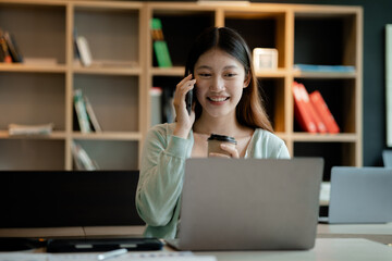 Beautiful Asian woman talking on the phone in the office of a startup company, she is a company finance employee working in the finance department. Concept of women working in a company.