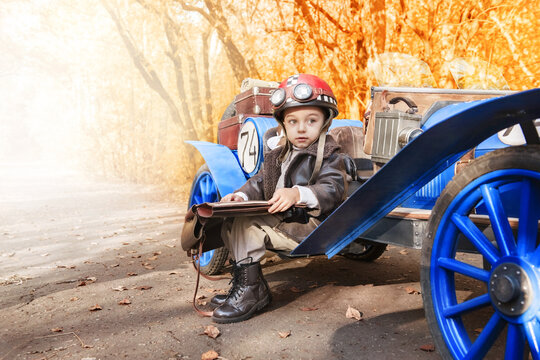 Young happy child. Little funny boy in the image of a racer started and plays an old racing car in an autumn park. Art photography of a kid in retro style.