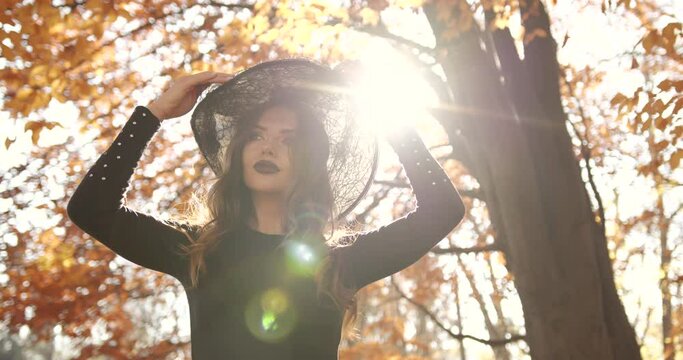 Attractive woman in a special dress and hat looks like a witch in the autumn forest