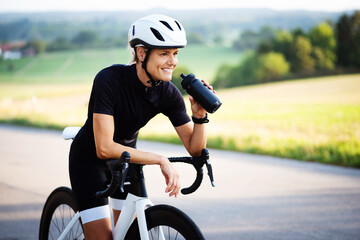 Rennradfahrer, sportliche Frau in Fahrradkleidung und mit Helm beim Sport - 528007021