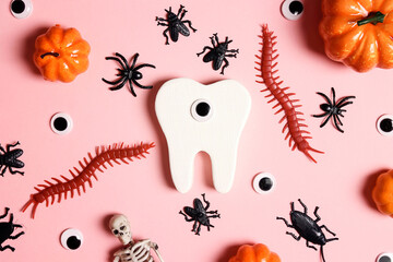 White funny creepy tooth with Halloween decorations on pink background.