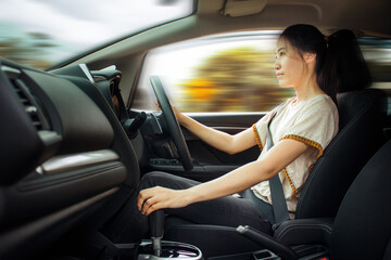 Fototapeta na wymiar Happy Asian woman driving a car and smiling. Cute young success happy brunette woman is driving a car. Portrait of happy female driver steering car with safety belt