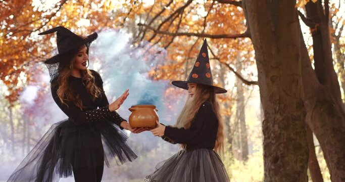 Beautiful brunette mom and cute little daughter looking like witches in special dresses and hats in autumn park
