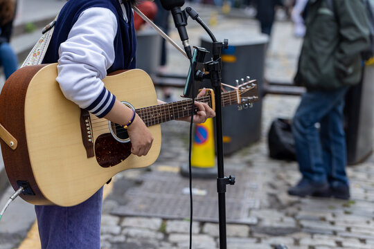 Busker. Singer guitarist street musician with acoustic guitar. Close up with selective focus on foreground.