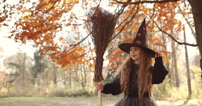 Cute little girl with long hair looking like a witch in a special dress and hat in the autumn forest