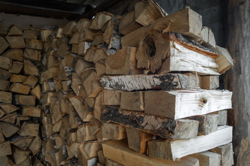 Split birch firewood for heating the home stove and fireplace in winter. Wooden wall from pile of firewood stacked in an shed. Preparation of the stock of firewood for the winter period. Selective