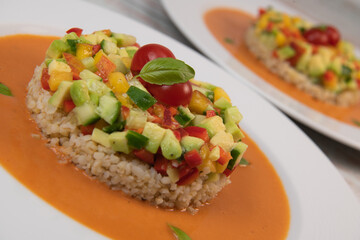 Vegan salad recipe based on bulgur with small vegetables, avocado, tomato, cucumber, pepper, nectarine fruit, tomato basil sauce and olive oil and lemon