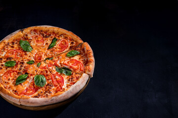 Delicious fragrant pizza-Margherita with mozzarella, tomatoes and basil on tomato sauce on black background. Copy space