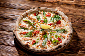 Pizza with salmon, mozzarella, cherry tomatoes, arugula, lemon and parmesan. Italian cuisine on a woden background