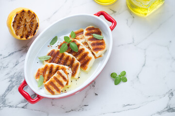 Serving pan with freshly grilled halloumi cheese on a white marble background, elevated view, horizontal shot with space