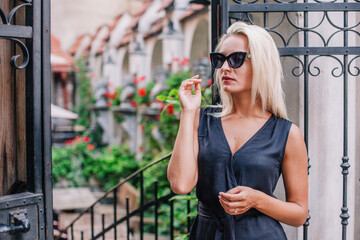 Fototapeta premium A young, blonde girl in a black blouse and sunglasses poses against the backdrop of an old courtyard in Lviv. Ukraine.