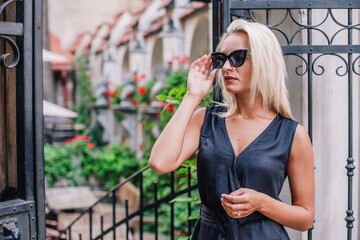 Fototapeta premium A young, blonde girl in a black blouse and sunglasses poses against the backdrop of an old courtyard in Lviv. Ukraine.