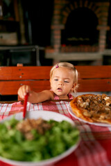 Little girl at the table reaches for a salad with her hand. High quality photo