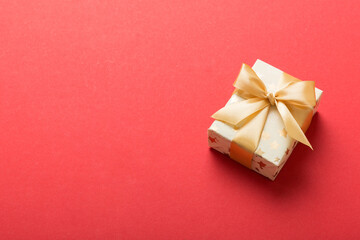 wrapped Christmas or other holiday handmade present in white paper with gold ribbon on colored background. Present box, decoration of gift on colored table, top view with copy space