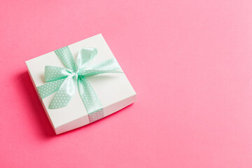 wrapped Christmas or other holiday handmade present in white paper with green ribbon on colored background. Present box, decoration of gift on colored table, top view with copy space