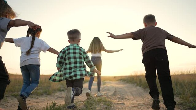 Happy group of children run on grass.Boys and girls on nature walk in summer.Smiling children play in park at sunset.Active friendly family have fun play in the park.Children run across grass together