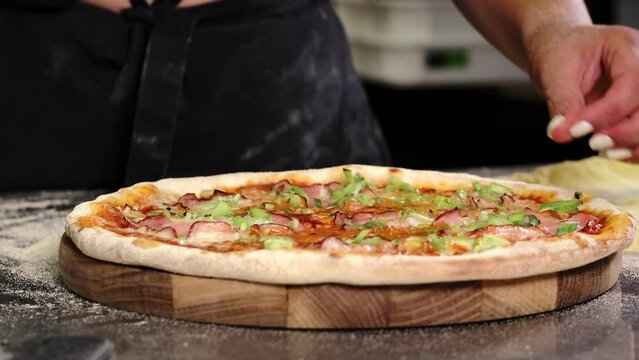 Freshly baked appetizing pizza with mozzarella cheese, ham, leeks on a tomato base cuting into slices with a pizza cutter for serving in a pizzeria.