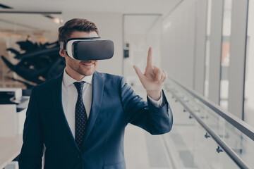 Smiling business professional in suit wearing VR headset on head using virtual reality at workplace