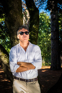 Young man is wearing sunglasses, a white shirt and bedge pants. Handsome businessman is working outdoors in the park.