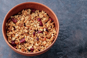 Granola with nuts and dried fruit on a dark background. Homemade granola in a clay bowl. Top view. Copy space
