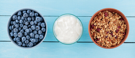 Blueberries, yogurt and granola in bowls. Berries, baked granola and fresh yogurt on blue boards. Healthy breakfast ingredients. Top view