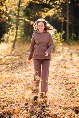 Young woman in hoodie sweater walking in autumn park. Sunny weather. Fall season.
