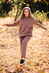 Young woman in hoodie sweater walking in autumn park. Sunny weather. Fall season.