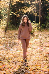 Young woman in hoodie sweater walking in autumn park. Sunny weather. Fall season.