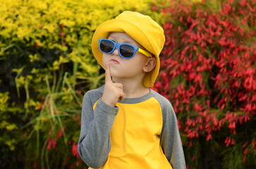 Portrait of a little boy in the garden. A child in a bright yellow Panama hat and a yellow sweater....