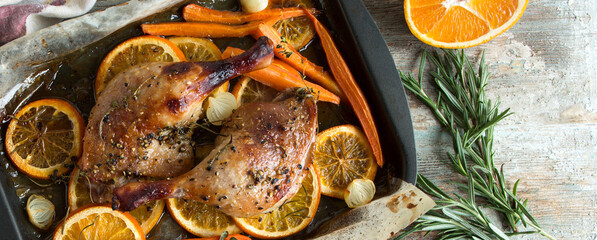 baking sheet with baked duck legs with carrots and oranges on the table
