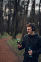 Redhead young man using a smartphone while running in the forest