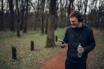 Redhead young man using a smartphone while running in the forest