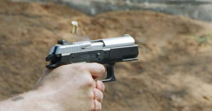 Close up footage of a hand gun firing in a firing range with cartridge flying away