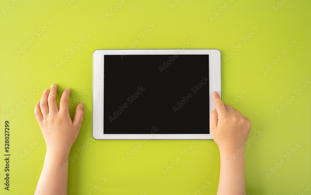 Wall mural high angle shot of a little kid using a digital tablet with tablet computer on green background in h