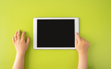 High angle shot of a little kid using a digital tablet with tablet computer on green background in...