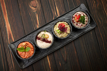 A variety of vegetable appetizers, on black plates on a wooden background