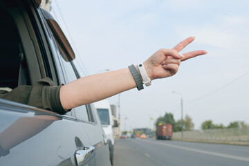 Woman driver put her hand out the open window and showing two fingers up. Driver gesture on the road. Person driving a car and showing sign of victory or peace.