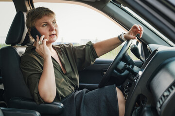 Middle-aged woman with a short haircut sits behind the wheel of a car and speaks indignantly on the...