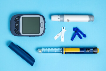Measuring blood sugar. Glucometer, insulin pen, lancet and test strip on a blue background.