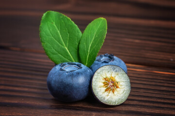 fresh Blueberries with cut in half and green leaves on wooden background.