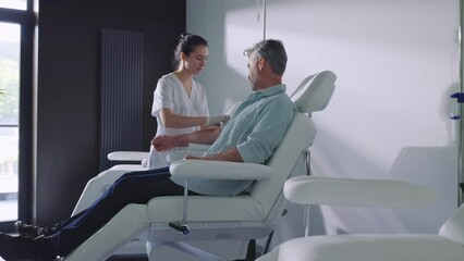 Close up in a modern clinic doctor preparing taking blood from the patient in light room. Female nurse and patient man sitting talking smiling. Slow motion