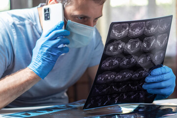 Doctor in mask attentively examines MRI and calling pacient