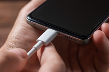 Charging a smartphone via a USB cable and a power supply. A black smartphone hanging with a usb charging cable.