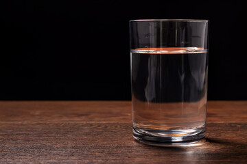 Water glass on wooden table on dark background