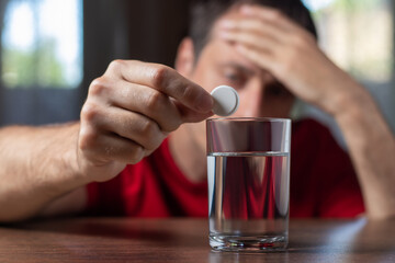 Man taking medicine for hangover at home, focus on hand with pill
