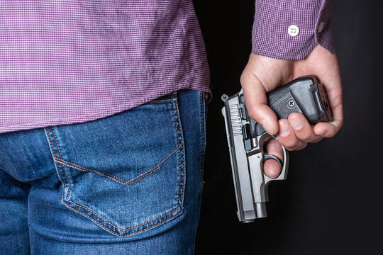 A man holding a gun in his hand behind his back, close-up view. Concepts: crime, attempted murder, a gunshot wound